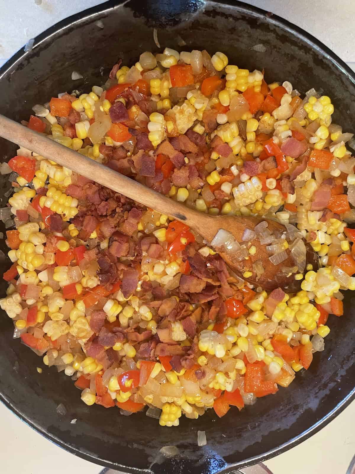 Corn Bread Pudding mixing in corn and bacon in skilet