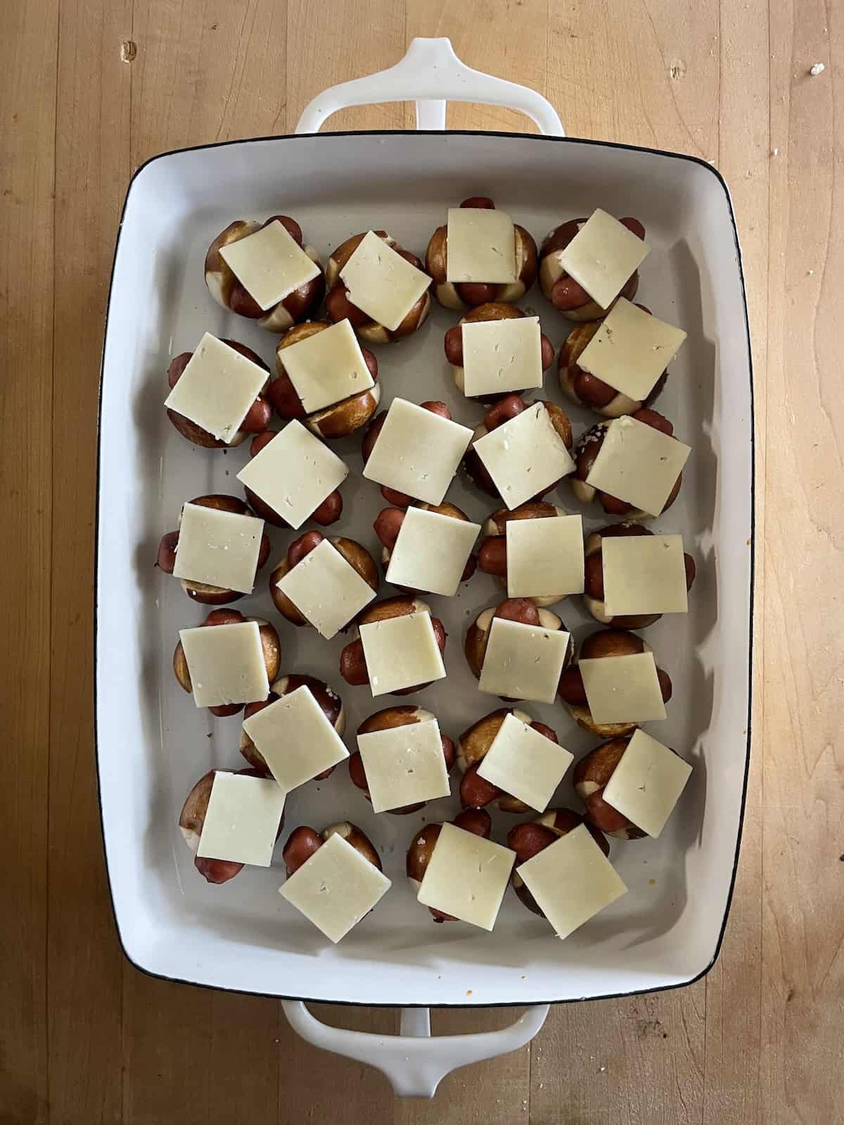 Little Smokie Pretzel Bites with Honey Mustard and Apple Jelly in baking dish topped with cheese