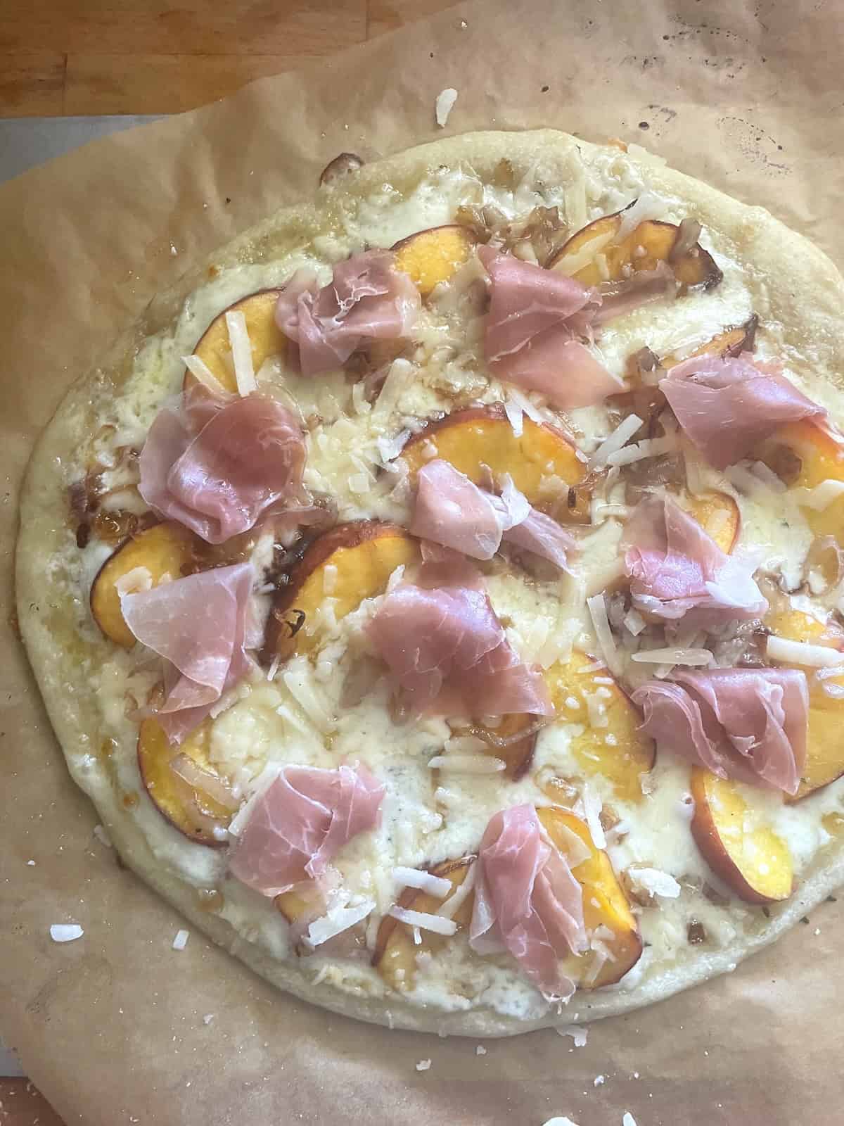 half baked pizza topped with grand padano and prosciutto